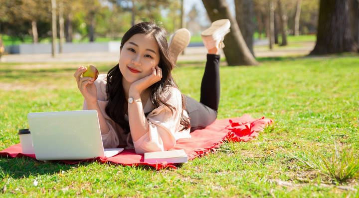 Relaxed Asian woman holding apple and using laptop on lawn